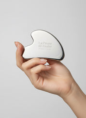 Main féminine tenant un Gua Sha en acier inoxydable pour massage du visage