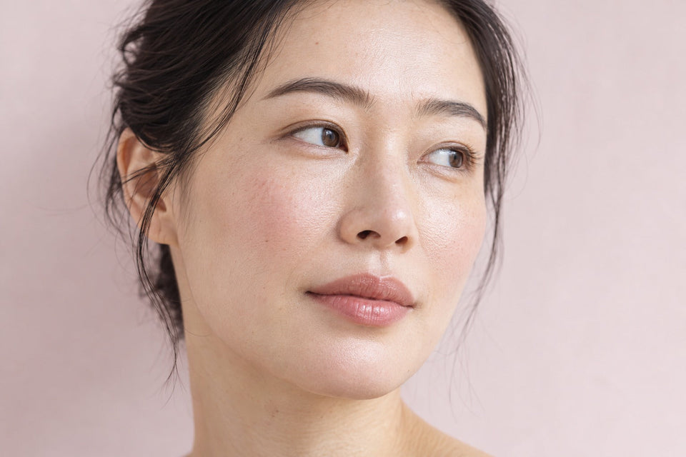 Portrait rapproché d’une femme aux joues légèrement rosées sur un fond rose clair.