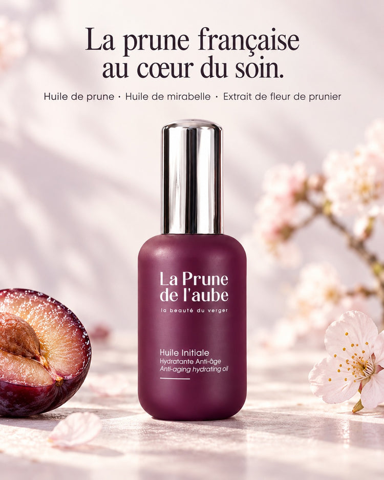 Flacon de l’Huile Initiale accompagné d’une prune violette. La prune française au cœur du soin. — Huile de prune · Huile de mirabelle · Extrait de fleur de prunier